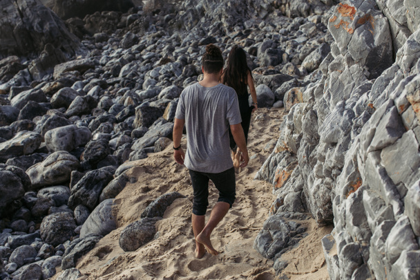 widok z tyłu mężczyzna chodzenie za kobieta na skalistej plaży w Portugalii - Zdjęcie, obraz