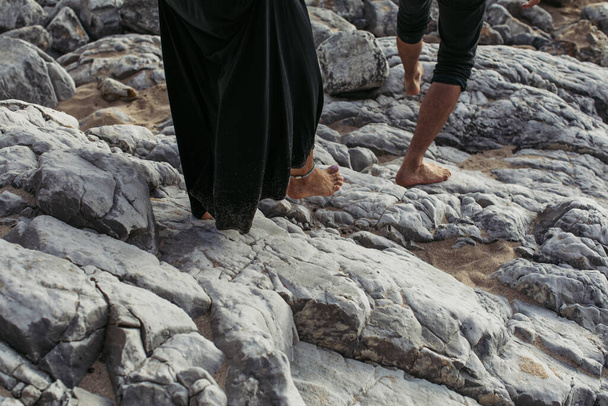 Ausgeschnittene Ansicht eines barfüßigen Mannes und einer barfüßigen Frau mit Knöchelarmband, die auf Felsen gehen - Foto, Bild