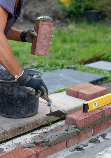 Construction work in progress. Male builder working with red bricks. Masonry wall close up photo.   - Photo, image