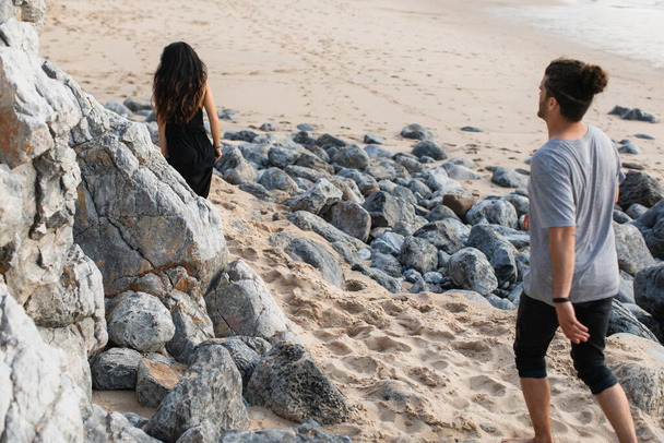 髭を生やした男がポルトガルの岩の多いビーチで女性の後ろを歩いていて - 写真・画像