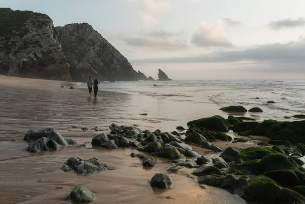 vrolijk man met uitgestrekte handen ontmoeting vriendin in hoed en jurk wandelen op nat zand in de oceaan  - Foto, afbeelding