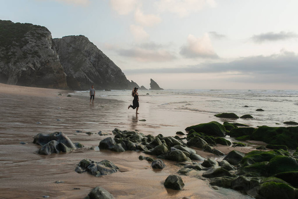 happy woman holding hat and running on wet sand near boyfriend   - Foto, Imagen