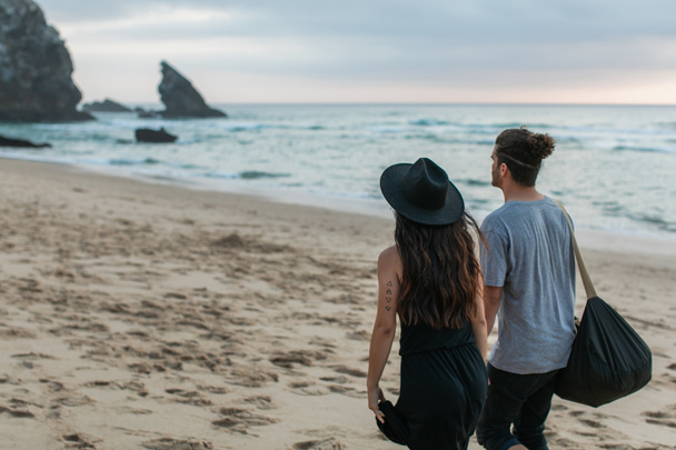 zpět pohled na tetovanou ženu a muže kráčející společně na písečné pláži - Fotografie, Obrázek