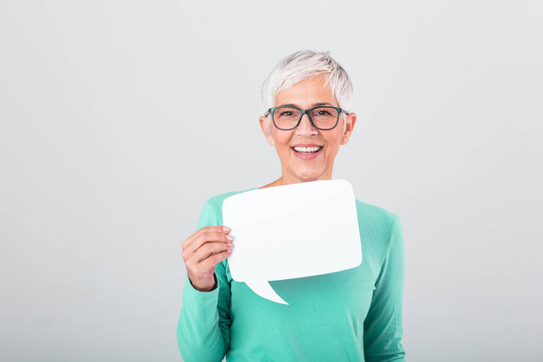 Happy mature woman in plain blue long sleeve t-shirt holding empty speech bubble isolated on background. Woman showing sign speech bubble banner looking happy - 写真・画像