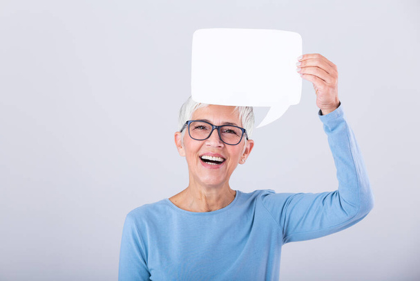 Portrait of a an excited mature gray hair woman showing blank speech bubble isolated over gray background. Senior woman holding speech bubble banner - Foto, Imagem