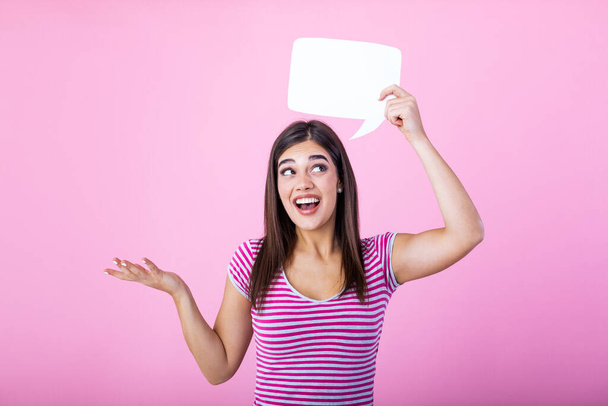 Young beautiful girl holding a bubble for text, isolated on a pink background. Young woman with smile holding blank speech bubble against background - Photo, image