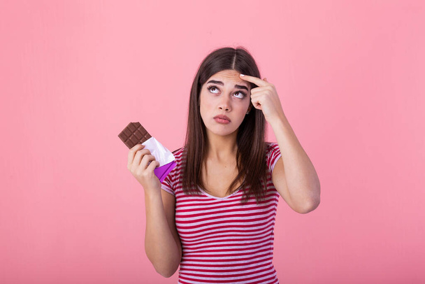 Teenage girl with acne problem holding chocolate bar against pink background. Young beautiful Woman Acne Problem Face with Chocolate bar UnHappy Eating,His Stressful face. - Foto, Imagen