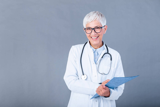 Happy smiling senior female doctor writing on clipboard, isolated on background. Medicine and health care concept. Smiling mature medical doctor woman with stethoscope. - Foto, Bild