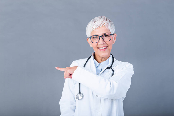 Doctor Mature woman, medical professional pointing in left direction isolated over gray background. Female mature doctor with stethoscope - Φωτογραφία, εικόνα