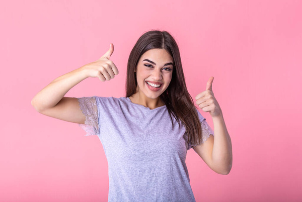 Smiling pretty young woman showing thumbs up isolated on the pink background. Smiling woman showing thumbs up and looking at the camera - Foto, Imagem