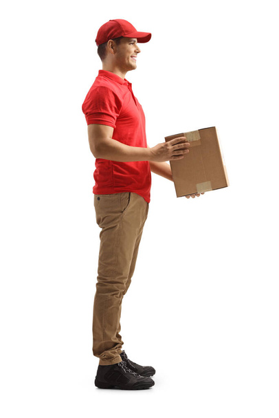Full length profile shot of a courier holding a cardboard box isolated on white background  - Fotó, kép