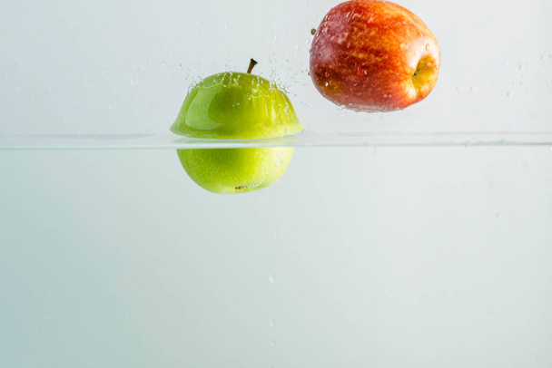 Close up view of red and green apples falling into water isolated on background. - Photo, Image