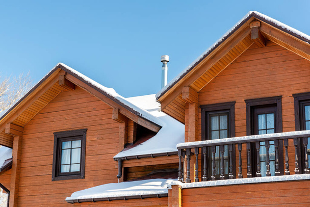 Scenery facade front view of modern wooden luxury timber eco house villa with garage door snowcapped by white fresh snow at cold sunny winter day. Real estate building construction project exterior. - Fotó, kép