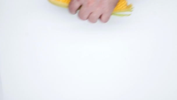 Las manos ponen maíz y cuchillo sobre un fondo blanco. Aislado. Un hombre pone maíz en la mazorca con hojas verdes y cáscaras y un cuchillo grande. Maíz fresco para cocinar. Comida saludable. De cerca. Vista superior - Imágenes, Vídeo