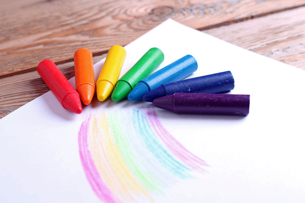 Oil pastel crayons lying on a paper with painted rainbow - Photo, Image