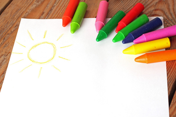 Масляные пастельные карандаши лежат на бумаге с раскрашенным детским рисунком
 - Фото, изображение