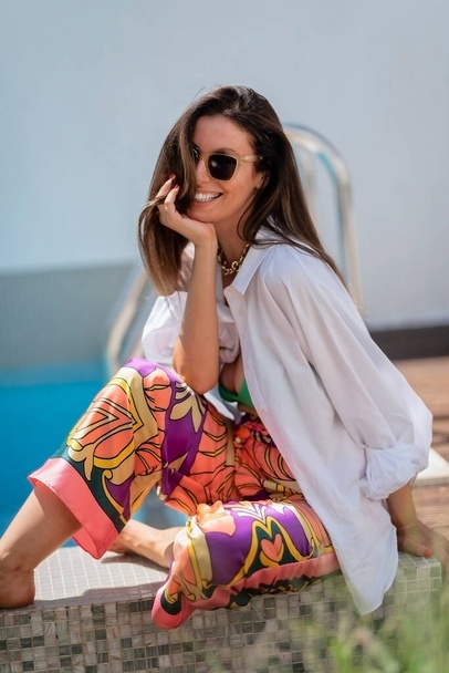 Portrait shot of attractive woman wearing sunglasses and beachwear while relaxing outdoor on a sunny day. - Foto, Imagen