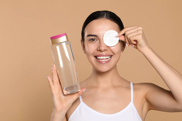 Young woman using cotton pad with micellar water on beige background - Photo, Image