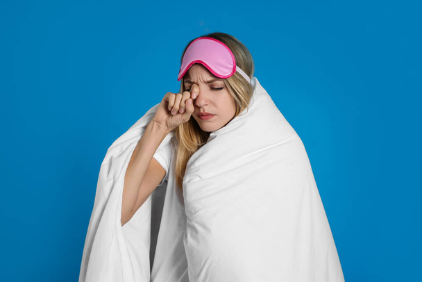 Young woman in sleeping mask wrapped with soft blanket on blue background - Foto, afbeelding