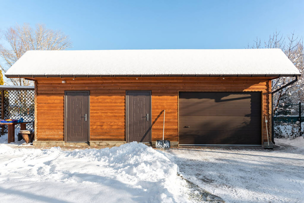 Facade front wall view closed door ATV home garage workshop clutter shed storage warehouse building snowy winter day. House organized warehouse tools equipment. Snow clean removal cold sunny weather. - Photo, image