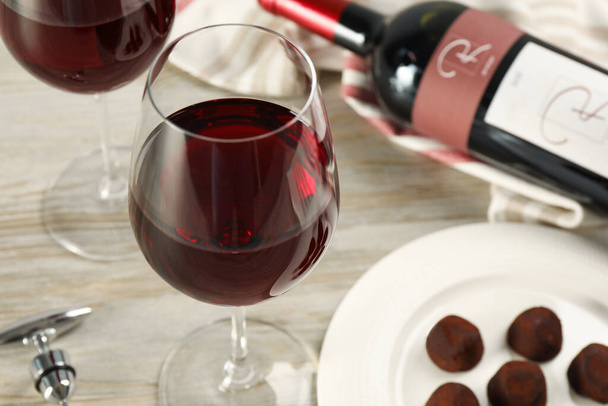 Glass of red wine with chocolate candies on white wooden table, closeup - Foto, afbeelding