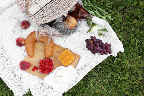 Picnic blanket with tasty food, flowers and cider on grass outdoors, flat lay - Fotografie, Obrázek