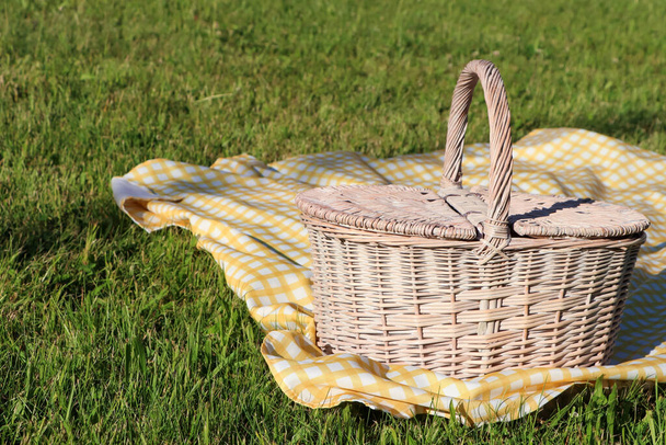 Picnic basket with checkered tablecloth on green grass outdoors, space for text - Foto, Bild