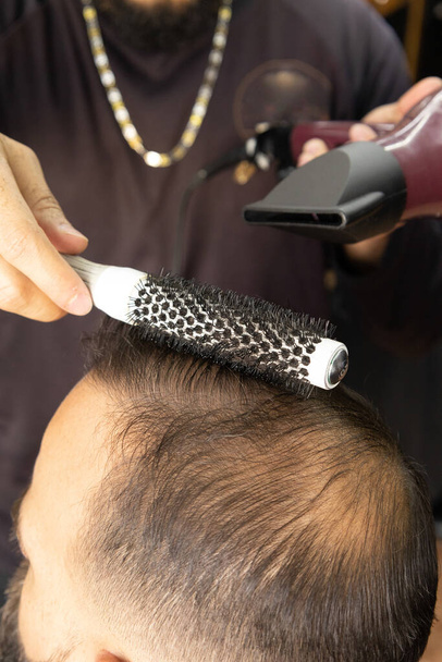le mani di un professionista che pettina una persona, usando un asciugacapelli e un pennello, dettagli di lavoro in un barbiere - Foto, immagini