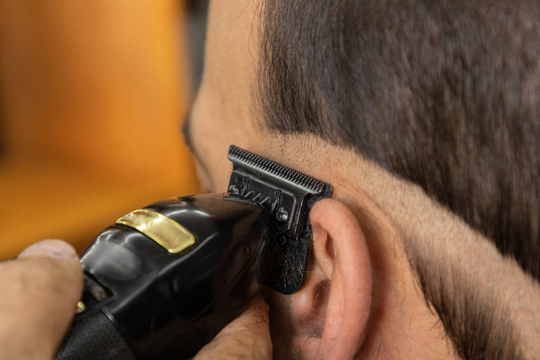 mani di un professionista che utilizza un rasoio per progettare un taglio di capelli moderno, dettagli del lavoro in un barbiere, cura del corpo, bellezza - Foto, immagini