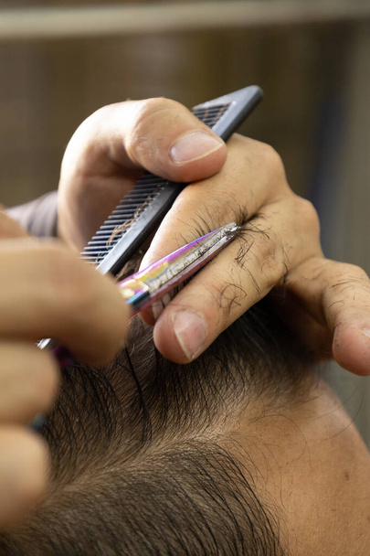 Bir insanın saçını makas, tarak ve parmak kullanarak kesen bir profesyonelin elleri. Berber dükkanındaki işin detayları, vücut bakımı, güzellik. - Fotoğraf, Görsel