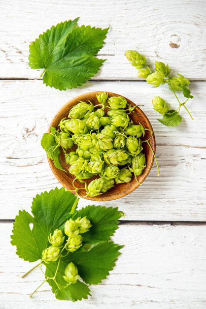 Picked herbal medicinal plant Humulus lupulus, the common hop or hops. Hops flowers in wood bowl on white wood background, indoors home. Flat lay view, copy space. - Fotografie, Obrázek