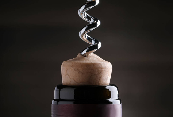Opening wine bottle with corkscrew on dark background, closeup - Fotó, kép