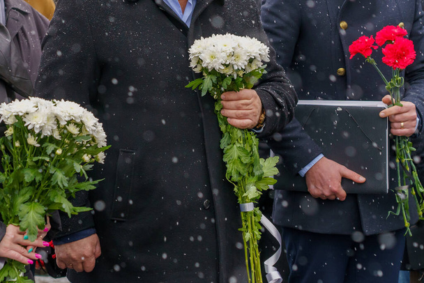 Λουλούδια στα χέρια σε μια επίσημη τελετή ωοτοκίας ή μια μνημόσυνο ημέρα πένθους σε κακές καιρικές συνθήκες το χειμώνα κάτω από το χιόνι. Ιστορικό με επιλεκτική εστίαση και χώρο αντιγραφής για κείμενο - Φωτογραφία, εικόνα