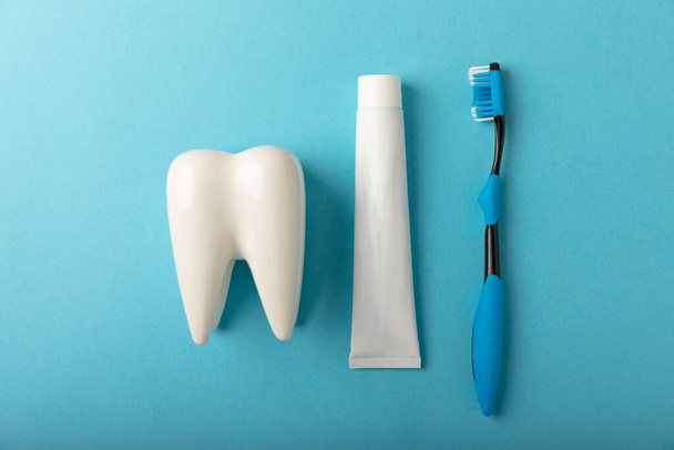 Toothbrush and toothpaste with tooth model on blue background with copy space. Flat lay. Oral hygiene. Oral Care Kit. Dentist concept. - Fotoğraf, Görsel