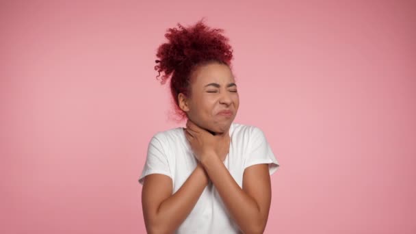 Sick sad young curly redhead African American woman touching neck feeling discomfort or pain. Unhealthy African female suffering from angina, sore throat or loss of voice on isolated pink background - Video