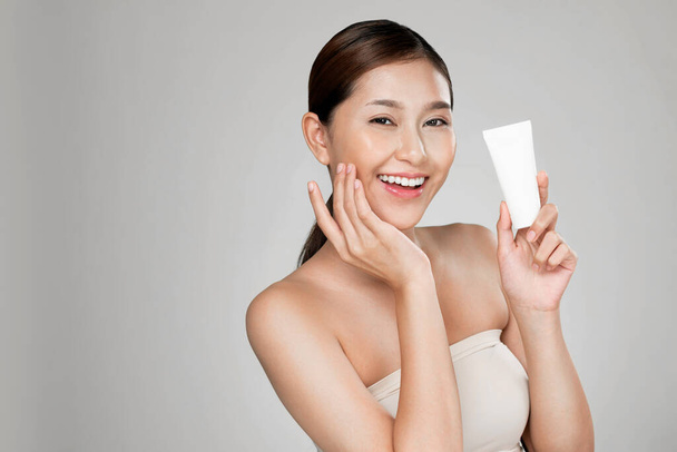 Ardent woman smiling holding mockup product for advertising text place, light grey background. Concept of healthcare for skin, beauty care product for advertising. - Foto, afbeelding