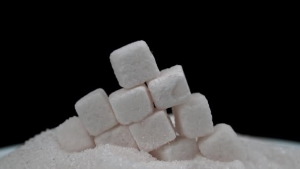 White sugar cubes fall on granulated sugar on a black background. The sugar spreads evenly. Benefits or harms of sugar consumption for health. - Filmati, video