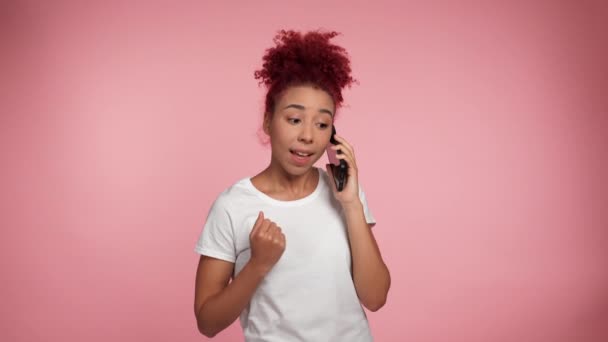 Portrait smiling curly redhead African American woman talking on mobile cell phone is happy found job or admission to university, great big win news winner gesture say yes on isolated pink background - Кадри, відео