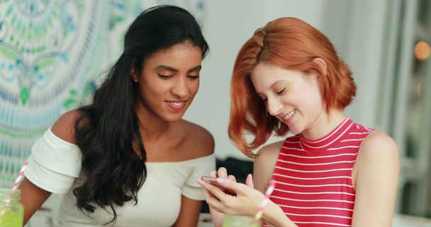 Zwei multiethnische Mädchen blicken lachend auf den Handybildschirm - Foto, Bild