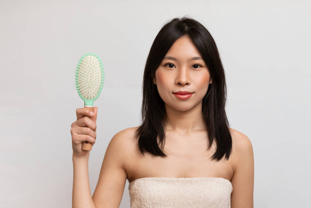 Healthy and beautiful hair concept. Young asian lady with silky dark hair holding brush and looking at camera, posing over white studio background - 写真・画像