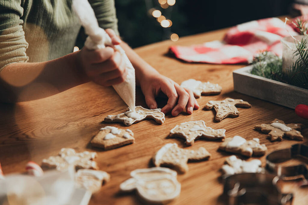 Christmas food preparation. Gingerbread cooking, decorating freshly baked cookies with icing and mastic. Little girl decorate cookie. Closeup on cropped shot with toddler kid hands holding icing pack - Foto, imagen
