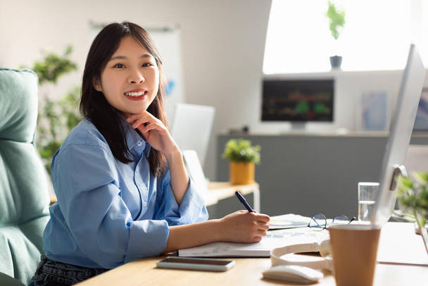 Successful Japanese Businesswoman Using Computer Working Online Smiling Posing Looking At Camera Sitting At Workplace In Office. Female Entrepreneurship And Business Career Concept. Side View - Φωτογραφία, εικόνα