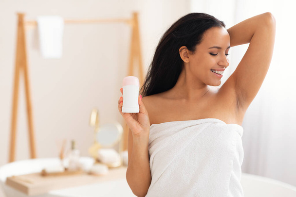 Happy Millennial Woman Holding Antiperspirant Stick Raising Arm Showing Smooth Armpit Standing Wrapped In Towel In Modern Bathroom At Home, Sweat Protection And Body Care - Φωτογραφία, εικόνα