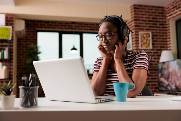 Young african american woman in wireless headphones watching movie online on streaming service on laptop, freelancer having break from work. Teenager leisure activity, home entertainment - Foto, afbeelding