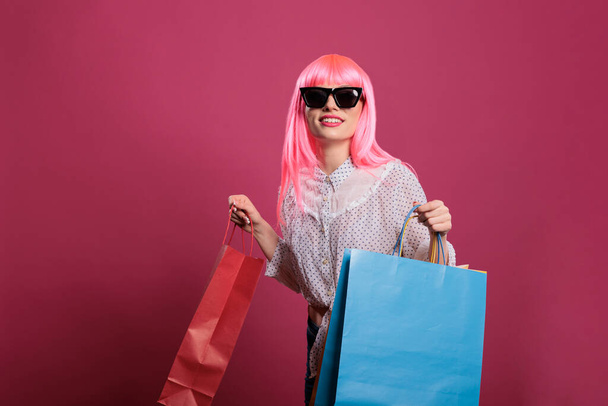 Stylish person with sunglasses carrying shopping bags after buying clothes from retail store at mall, using sale discount purchase. Fashionable customer feeling happy after paying money on package. - Foto, imagen