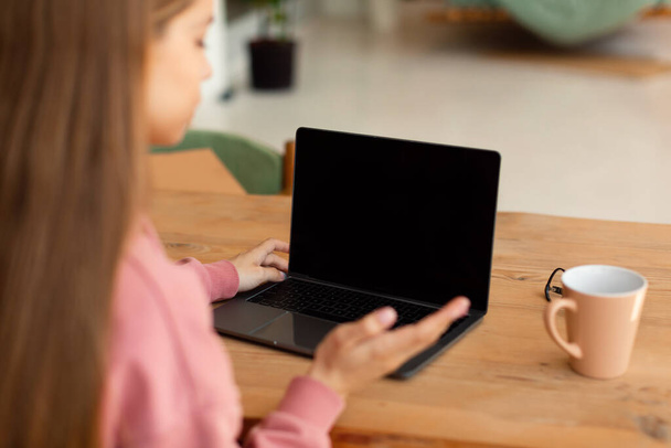 Над плечем знімок невпізнаваної дівчини-підлітка сидить за столом і використовує ноутбук з порожнім екраном, має відеодзвінок з учителем, макет, крупним планом
 - Фото, зображення