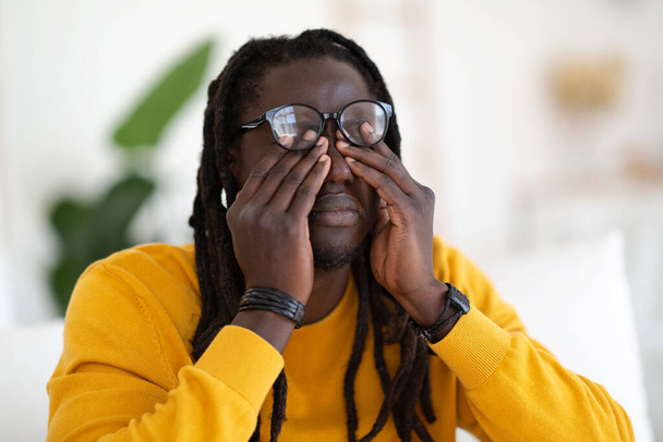 Portrait Of Tired Young Black Man Rubbing Eyes Under Eyeglasses, Exhausted African American Guy Having Poor Eyesight, Suffering From Eyestrain While Sitting On Couch At Home, Closeup Shot - Foto, Imagen
