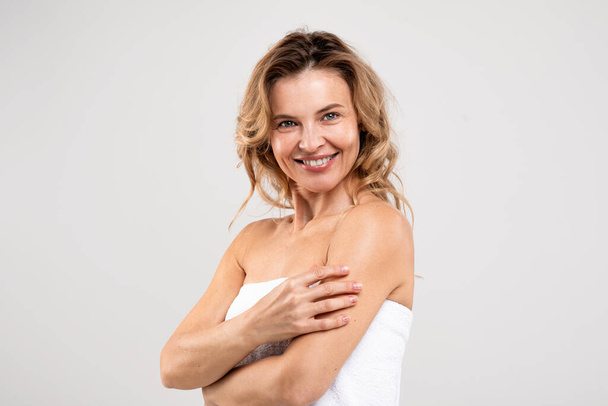 Natural Beauty. Portrait of cheerful middle aged female with beautiful skin standing wrapped in bath towel over light studio background, attractive woman enjoying self-care routine, free space - Φωτογραφία, εικόνα