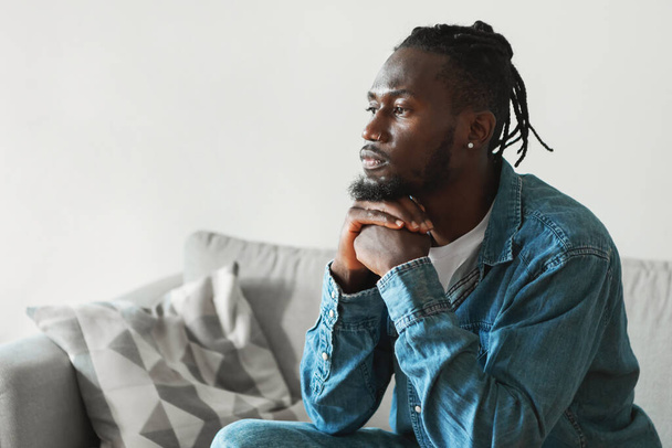 Serious African American Man Thinking Sitting On Sofa At Home, Looking Aside. Side View Shot Of Concerned Millennial Guy Thinks About Problems Suffering From Depression. Male Mental Health - Foto, imagen