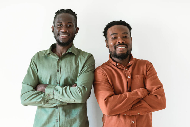 Two Smiling Black Men Posing Standing Crossing Hands Looking At Camera Over White Background. Studio Shot Of Male Friends Expressing Positive Emotions. Confidence And Friendship Concept - Photo, image